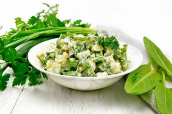 Salad of cucumber, sorrel, boiled potatoes, eggs and herbs, dressed with mayonnaise in a white plate, parsley, green onions and towel against the background of wooden boards