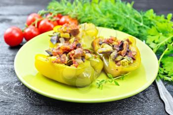 Sweet pepper stuffed with mushrooms, tomatoes, zucchini, eggplant and onions, seasoned with wine, garlic, thyme and spices in a green plate on wooden board background