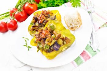 Sweet pepper stuffed with mushrooms, tomatoes, zucchini, eggplant and onions, seasoned with wine, garlic, thyme and spices in a white plate on a kitchen towel against wooden board