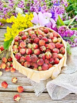 Wild ripe strawberries in a bark box with parchment, burlap and wild flowers on a wooden board background