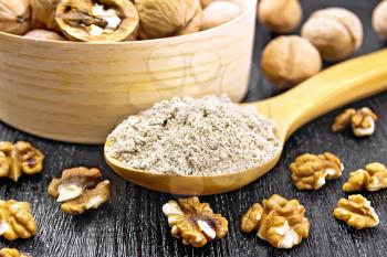 Walnut flour in a spoon, nuts in bowl and on table on background of dark wooden board
