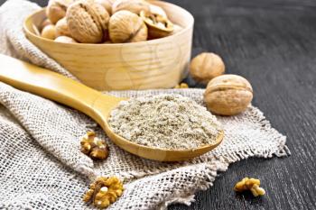 Walnut flour in a spoon on burlap, nuts on a table and in a bowl on wooden board background