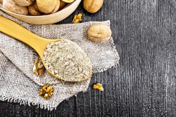 Walnut flour in a spoon on burlap, nuts on a table and in a bowl on wooden board background from above