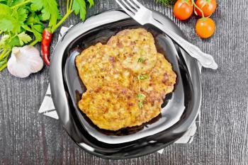Fritters of minced meat in a plate with a fork on napkin, garlic, parsley and hot pepper on black wooden board background from above