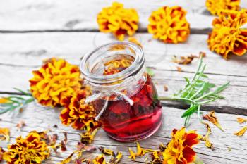 Alcohol tincture of marigolds in a glass jar, fresh and dried flowers with green leaves on background of an old wooden board