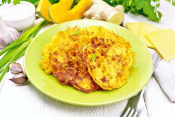 Fritters of pumpkin and cheese with ginger in a green plate, sour cream in a bowl, napkin, parsley and fork on white wooden board background