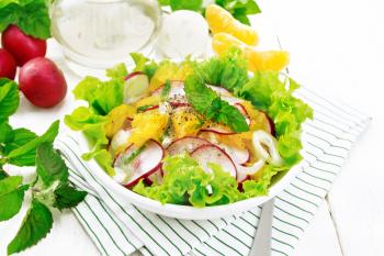 Radish, onion and orange salad with mint, vegetable oil and spices on lettuce in a plate on towel against a light wooden board