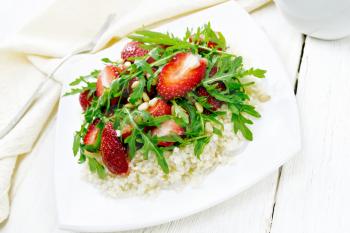 Strawberry, couscous, cedar nuts and arugula salad dressed with balsamic vinegar and olive oil in a plate, towel and fork on wooden board background
