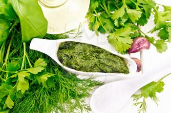Sauce of dill, parsley, basil, cilantro, other spicy herbs, garlic and vegetable oil in a gravy boat, a spoon with coarse salt on wooden board background from above