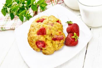 Strawberry scones in a plate with berries, a towel, mint, milk in jug and glass on wooden board background