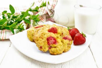 Strawberry scones in a plate with berries, a towel, mint, milk in jug and glass on white wooden board background