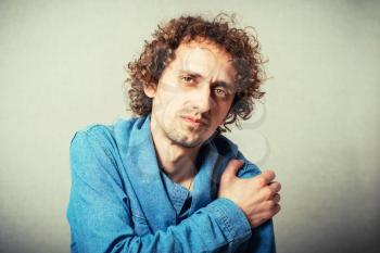 Curly young man aching shoulder. On a gray background