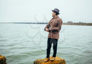 young man playing ukulele on stones at the lake