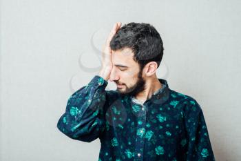 Bad morning. Frustrated young man holding his hand in hair and keeping eyes closed while standing against grey background