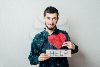 Closeup portrait of worried young man holding a help and a heart ! Human emotion facial expression