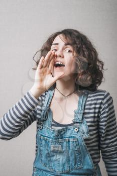A woman makes a gesture calling someone with hand near mouth. Gray background