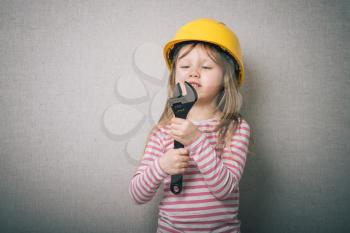 beautiful little girl in helmet with wrench isolated on gray background