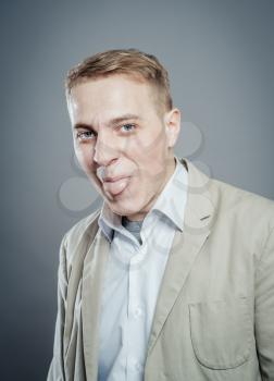 Closeup portrait funny annoyed young childish rude bully man sticking his tongue out at you camera gesture, isolated gray background. Negative emotion facial expression feelings, signs, symbols