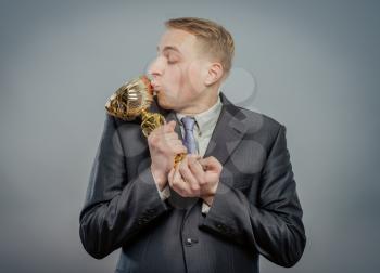 portrait of gesturing pride kiss businessman with gold cup. Concept of win and success