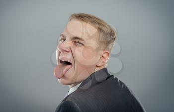 Closeup portrait funny annoyed young childish rude bully man sticking his tongue out at you camera gesture, isolated gray background. Negative emotion facial expression feelings, signs, symbols