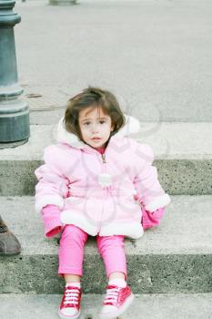Little girl in winter clothes sitting in stairs looking at the camera.