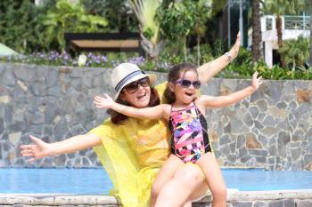 Mother and daughter happy in the pool with open arms enjoying the summer