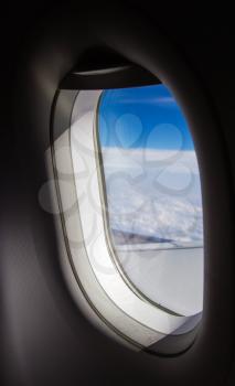 Plane window with blue sky and clouds outside.