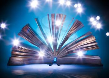Open old book, mystical blue light at background, light painting
