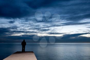 Man is standing on a jetty looking the sunset