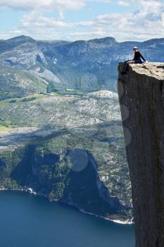 Royalty Free Photo of a Person Sitting on a Cliff in the Mountains of Norway