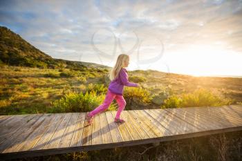 Little girl goes by boardwalk in sea shore at sunrise