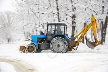 The tractor of dark blue color deletes snow in park