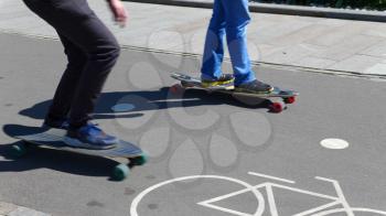 Feet of two boys riding on a skateboard ride on asphalt.