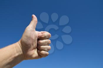 Hand of a man with a thumbs up gesture against a blue sky