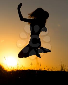 Silhouette of a girl jumping up at sunset .