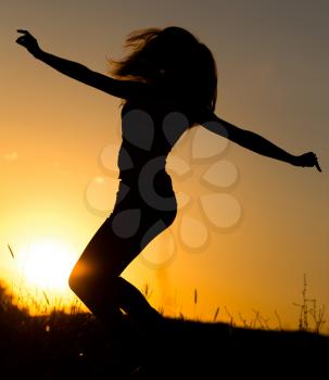Silhouette of a girl jumping up at sunset .
