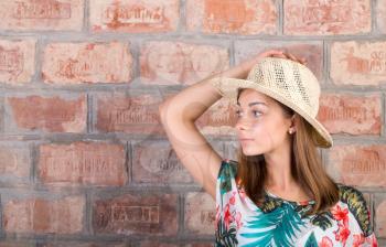 Portrait of a girl in a straw hat on a background of vintage brick wall