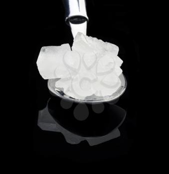 crystal sugar  on a spoon over black reflective surface background
