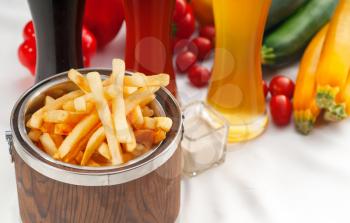 fresh french fries on a wood bucket with selection of beers and fresh vegetables on background