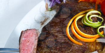 sliced fresh juicy beef ribeye steak grilled with orange and lemon peel on top and vegetables beside