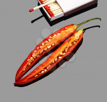 fresh red chili peppers  with matches over grey reflective surface