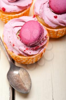 fresh pink berry cream cupcake with macaroon on top over rustic wood table