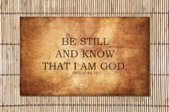 The bible Psalm scripture from 46:10 says Be still and know that I am God. Motivational and encouraging. Strong text over a stone background, with bamboo outside.