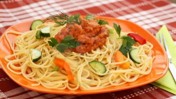 Spaghetti pasta with sauce and vegetables on table.