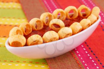 Potato rings and red sauce isolated on colorful tablecloth.