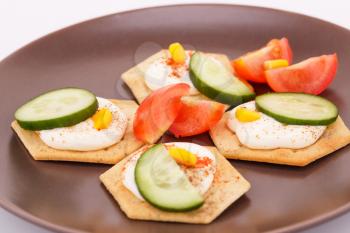 Snacks with vegetables and cheese cream on brown plate.