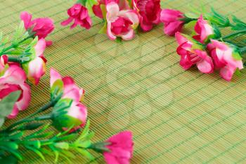 Pink fabric flowers on bamboo background, closeup picture.