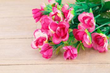 Pink artificial flowers on wooden background, closeup picture.