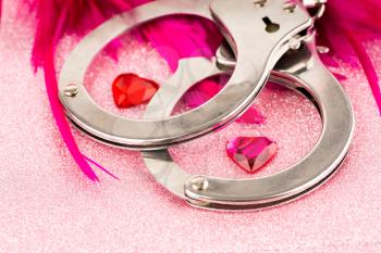 Handcuffs, pink feather and hearts on sparkling background.