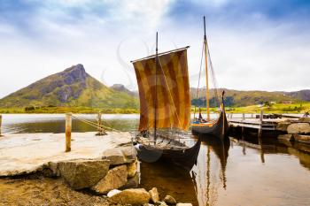 Landscape with viking boats at village small harbor, mountains and fjord in Lofoten islands, Norway.